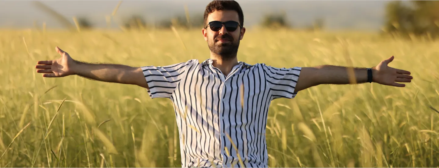 Man wearing sunglasses with arms spread standing in wheat field with grain heads starting to droop